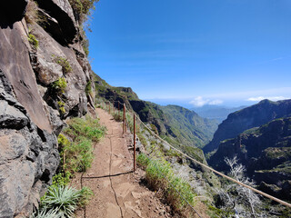 Fototapeta na wymiar Hiking trail on a beautiful sunny day. Rail for security. Amazing mountain path. Vibrant colors. Travel the world and discover its wonders. Madeira Island, Portugal. 