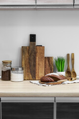 Wooden cutting boards, bread, jars with products, spoons and houseplant on table near light wall