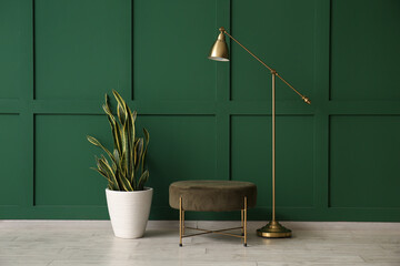 Modern lamp, houseplant and pouf near green wall