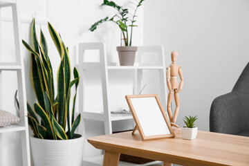 Blank frame, wooden mannequin and houseplant on table in room