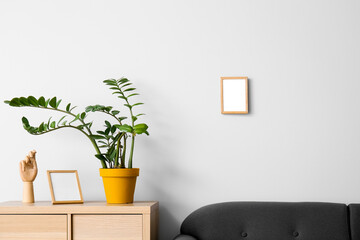 Blank frames, wooden hand and houseplant on  table with sofa near light wall