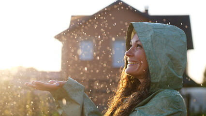 Young happy woman wearing green raincoat is feeling free and smiling under the rain. Concept of...
