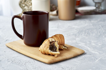Obraz na płótnie Canvas a coffee mug and a croissant broken in half on a cutting board