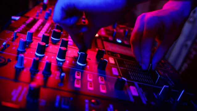 Professional confident DJ is adjusting fader on digital music console in neon light in nightclub. Male hand controls modern digital DJ console, closeup. Concept of music on neon party
