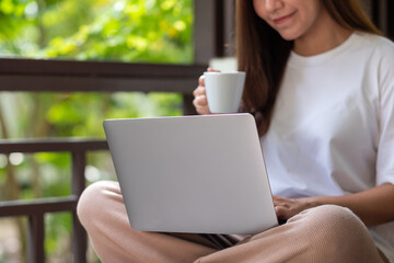 Closeup image of a young woman drinking coffee while using laptop computer for working or studying online at home