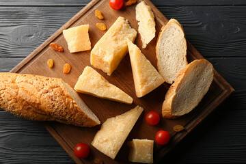 Fototapeta premium Board with pieces of tasty Parmesan cheese and bread on black wooden background