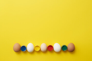 Chicken eggs and paints on a yellow background for easter