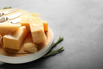 Wooden board with pieces of tasty Parmesan cheese on black background, closeup