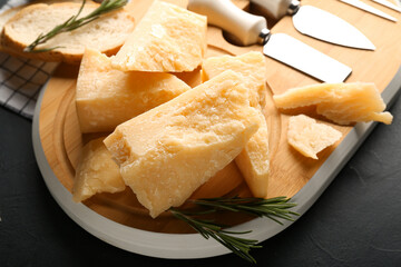 Wooden board with pieces of tasty Parmesan cheese on table, closeup