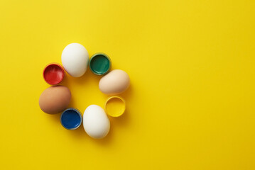 Chicken eggs and paints on a yellow background for colorful easter