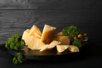 Wooden board with pieces of tasty Parmesan cheese on table