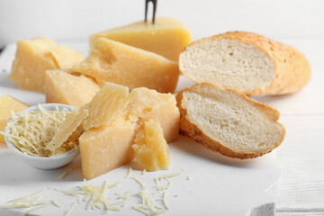Wooden board with pieces of tasty Parmesan cheese and bread on table