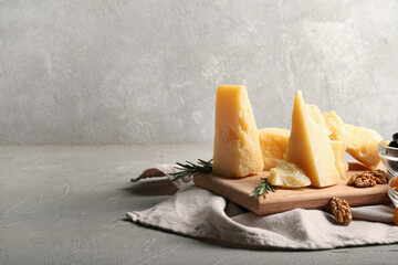 Wooden board with pieces of tasty Parmesan cheese on grey background