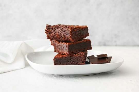 Plate with pieces of delicious chocolate brownie on light background