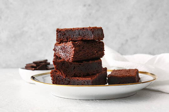 Plate with pieces of delicious chocolate brownie on light background