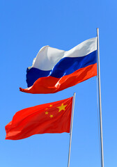 Flags of Russia and China are flying in the wind against the blue sky