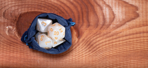 Set of role playing white dices in blue  storage bag on a gaming table made of wood: background for role-playing games with place for text, top view