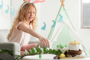 Fototapeta na wymiar Cute little girl with bunny ears taking Easter cake from table