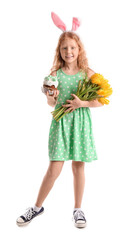 Funny little girl with bunny ears, flowers and Easter cake on white background