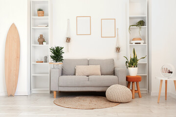 Interior of light living room with wooden surfboard, sofa and houseplants
