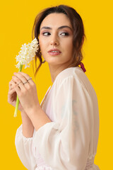 Pretty young woman with hyacinth flowers on yellow background