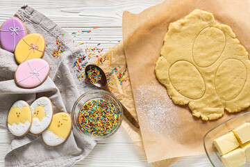 Fresh dough, sprinkles and Easter cookies on white wooden background