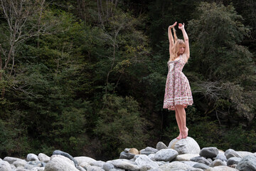 Beautiful sexy blond young woman in dirndl fashion stands like a statue in dry mountain river bed...