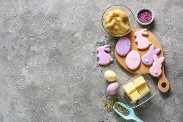 Wooden board with tasty Easter cookies and ingredients on grey background