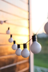 Garland of white light bulbs hanging on  wooden terrace in summer evening