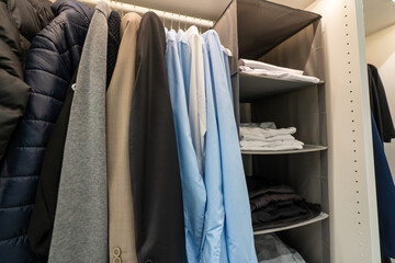 Modern style wooden cabinet with shirts, clothes and other items hanging on slide out rail. Wardrobe interior design concept.