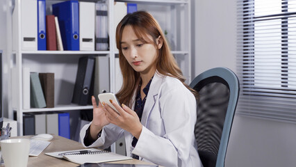portrait woman doctor seated at desk is pondering with a serious look while sliding the phone...