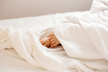 Little toddler's feet, wrapped in a towel, kid lying in bed