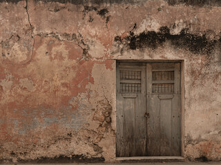 Old grunge cracked concrete wall with some stains and holes. White brown and orange collors. with old door
