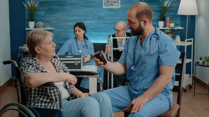 Man nurse giving bottle of pills to old patient with disability for healthcare treatment in nursing home. Senior woman in wheelchair receiving flask with medicine for medical recovery