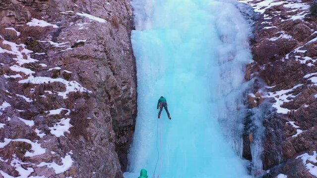 Man is leading on Ice. Ice Climbing on Frozen Waterfall, Aerial View. Barskoon Valley, Kyrgyzstan. Drone Flies Upwards, Tilt Down. Crane Shot