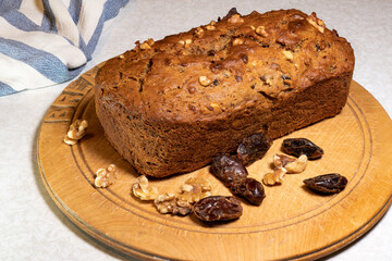 A freshly made homemade date and walnut loaf cake on an old breadboard with dates and nuts around it