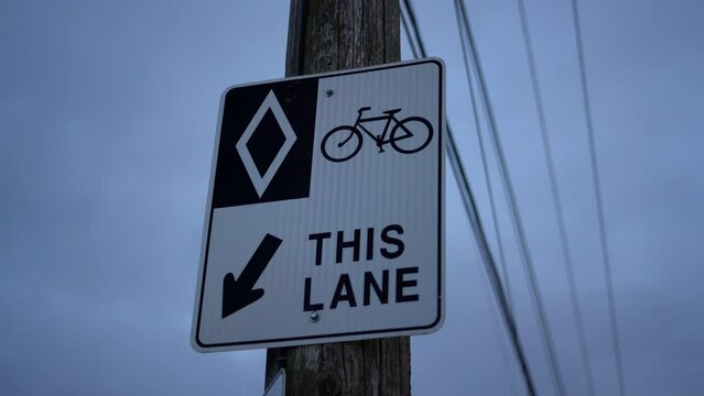 HOV bike lane diamond sign on wooden post in urban area with exposed telephone wires and electricity lines - sign for bikers, cyclists, and bicyclists - road rules and signs for bicycles on cloudy day