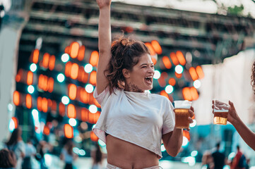 Beautiful woman drinking beer and having fun on a festival with her friends - obrazy, fototapety, plakaty