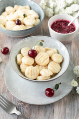 Traditional Ukrainian lazy cottage cheese dumplings served with sour cream and cherry sauce and fresh cherries on a wooden background.