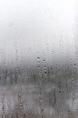 Vertical natural background, condensation on glass with drops flowing down, humidity and foggy blank. Outside , bad weather, rain