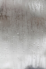 Condensation on glass with drops flowing down, Vertical natural background, humidity and foggy blank. Outside , bad weather, rain