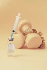 syringe is stuck in jar, dumbbells and measuring tape on yellow background are lying next to it, a...