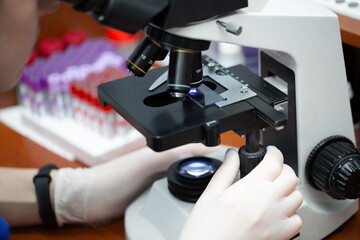 Young attractive veterinary worker in gloves using microscope for testing blood samples of animals. Vet doctor looking into microscope, close-up.