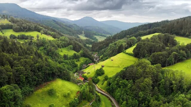 Flight over an idyllic green valley in the Black Forest (Schwarzwald), Germany. With forests, meadows on hills and a few houses in soft light
