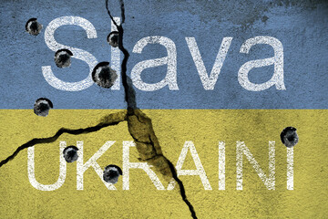 Slava UkrainI written on concrete wall with bullet holes and the ukrainan national flag. To...