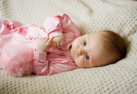 Little newborn baby girl lying on her tummy in pink clothes on a beige blanket.