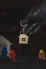 Human hand in black gloves is keeping key holder in a shape of a house.