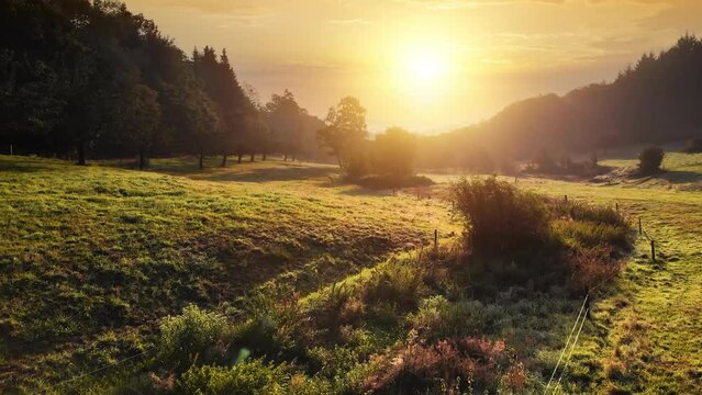 The sun rising over beautiful rural landscape surrounded by forests, creating dramatic warm sunrise colors 
