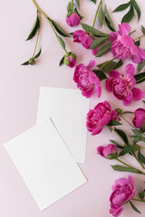 Blank paper invitation cards with copy space. Pink peony flowers bouquet on neutral pastel elegant pink background. Flat lay, top view minimal floral composition