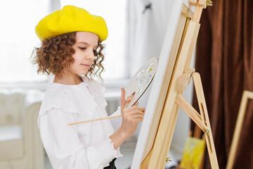 Little girl painting a picture in a studio or art school. Creative pensive painter child paints a colorful picture on canvas in workshop. Talented kids